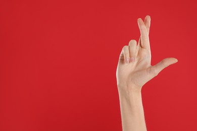 Woman with crossed fingers and space for text on red background, closeup. Superstition concept