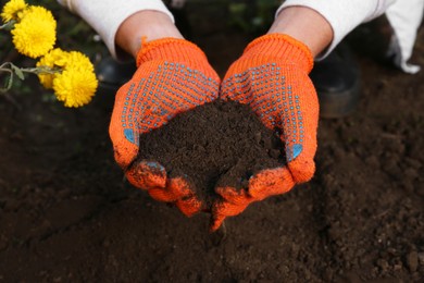 Woman in gardening gloves holding pile of soil outdoors, closeup