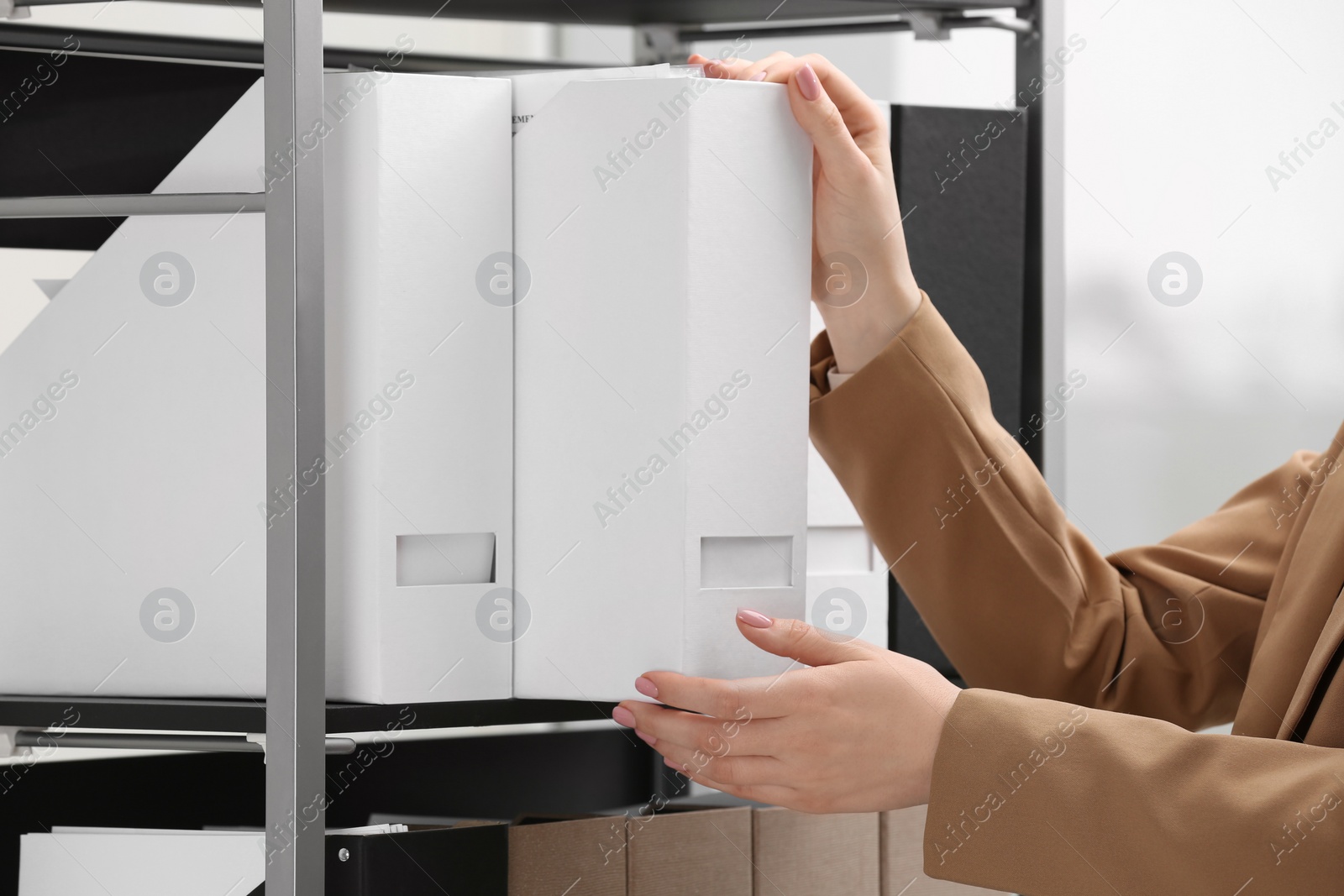 Photo of Woman taking folder with documents from shelf in office, closeup