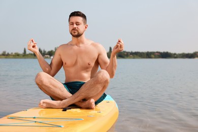 Photo of Man practicing yoga on SUP board on river, space for text