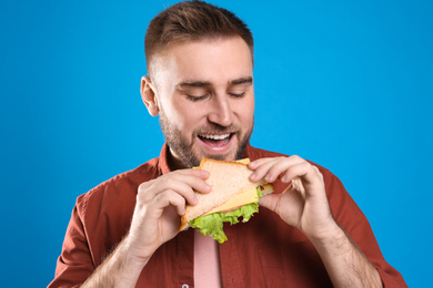 Young man eating tasty sandwich on light blue background