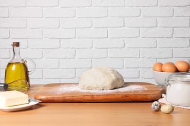 Fresh dough sprinkled with flour and other ingredients on wooden table near white brick wall
