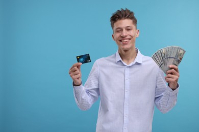 Photo of Happy man with credit card and dollar banknotes on light blue background. Space for text