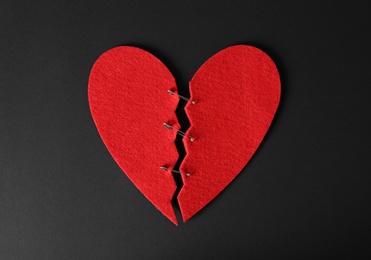 Photo of Halves of cut felt heart joined with pins on black background, top view