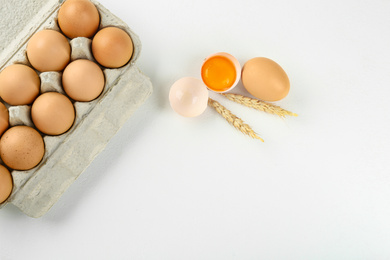 Photo of Raw chicken eggs and wheat spikes on white table, flat lay. Space for text