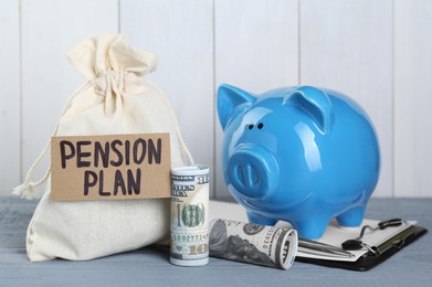 Photo of Card with phrase Pension Plan, sack, dollar banknotes and piggy bank on light blue wooden table. Retirement concept