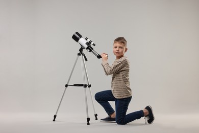 Cute little boy with telescope on light grey background