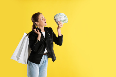 Emotional young woman with money and shopping bags on yellow background. Space for text