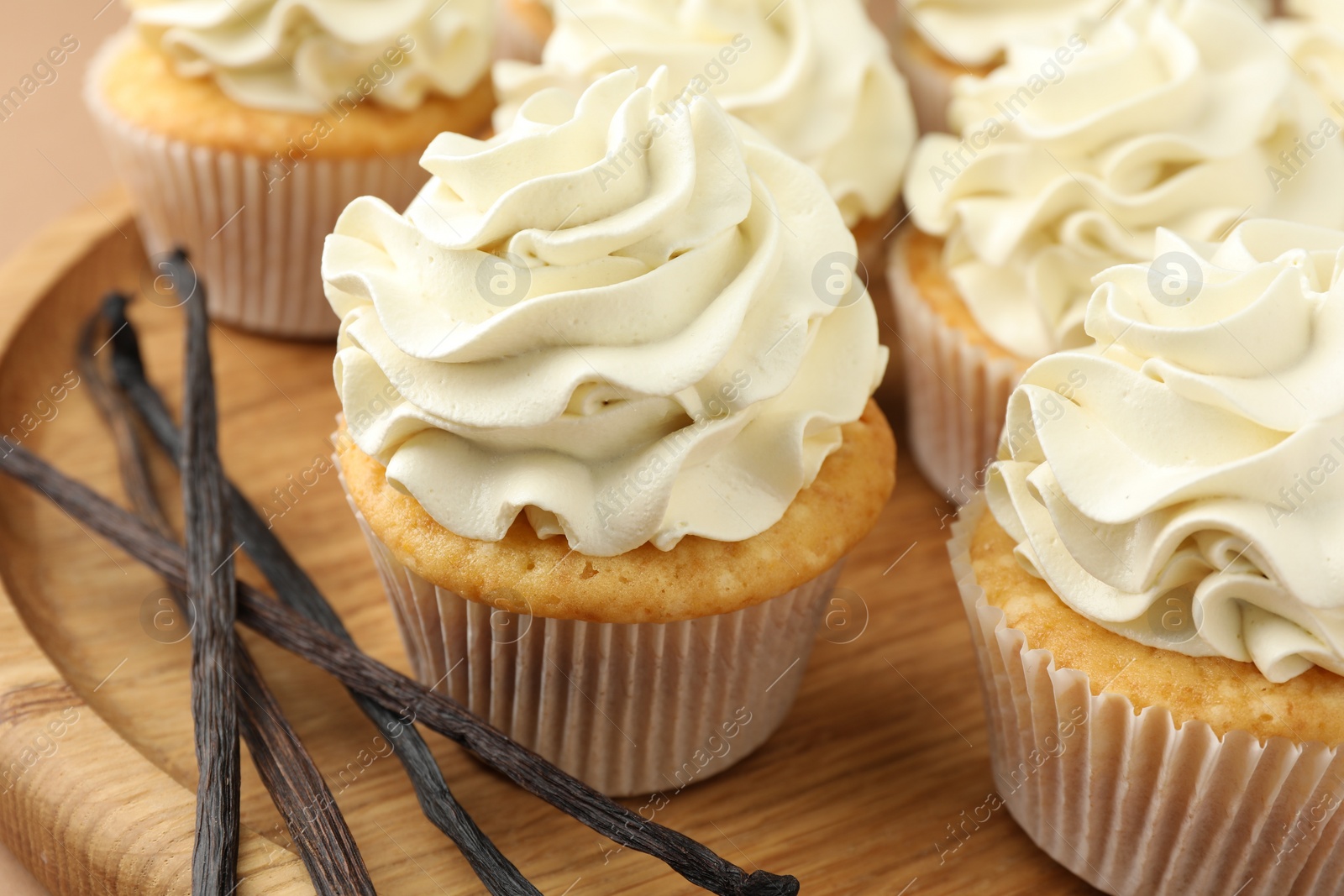 Photo of Tasty cupcakes with cream and vanilla pods on beige table, closeup