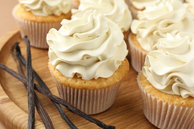 Photo of Tasty cupcakes with cream and vanilla pods on beige table, closeup