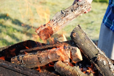 Photo of Man putting wood into metal brazier outdoors, closeup