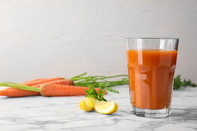 Glass of carrot drink and lemon slices on marble table, space for text