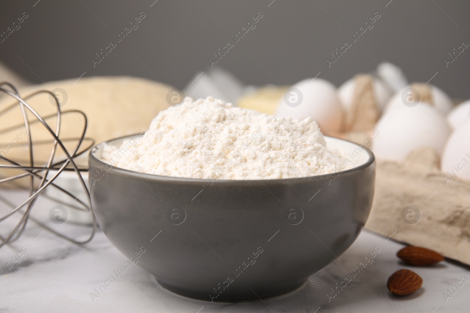 Photo of Bowl with flour on white marble table, closeup