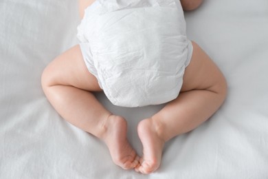 Photo of Cute little baby in diaper on bed, top view