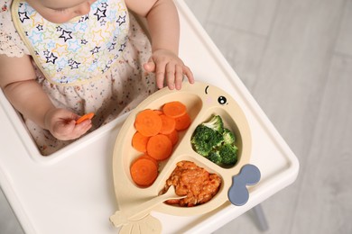 Little baby eating food in high chair indoors, closeup. Above view