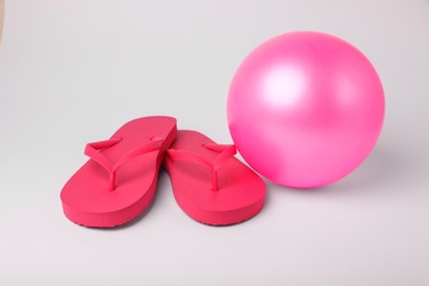 Photo of Pink inflatable beach ball and flip flops on white background