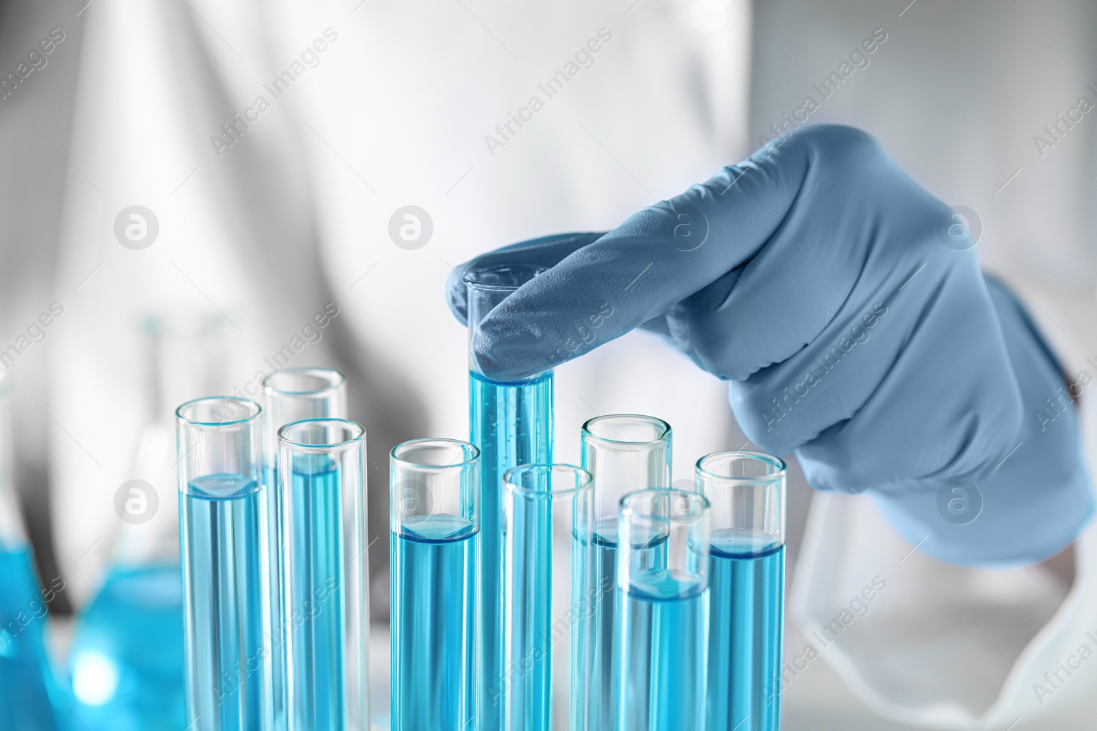 Photo of Scientist taking test tube with light blue liquid in laboratory, closeup