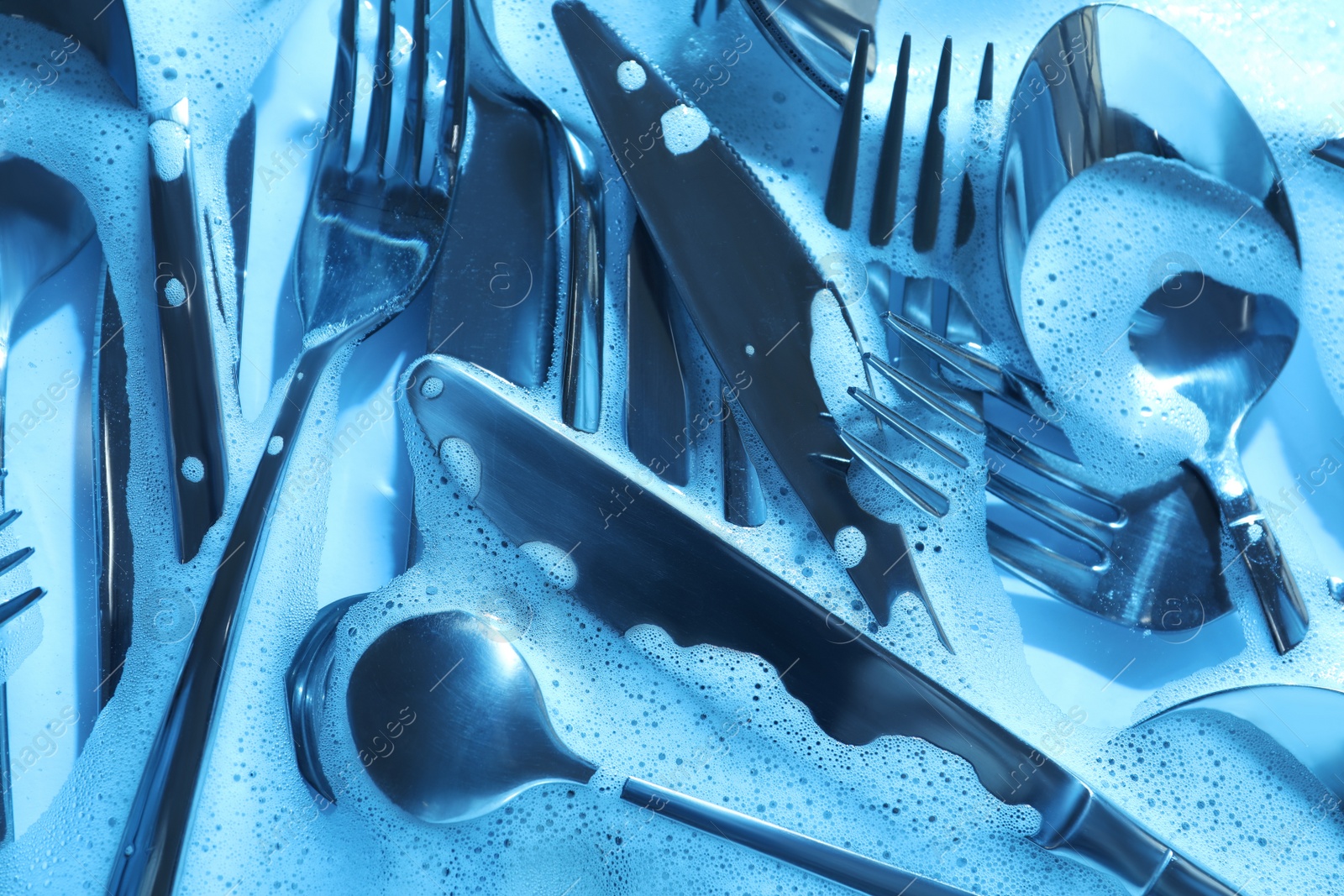 Photo of Different silverware in foam, flat lay. Toned in blue