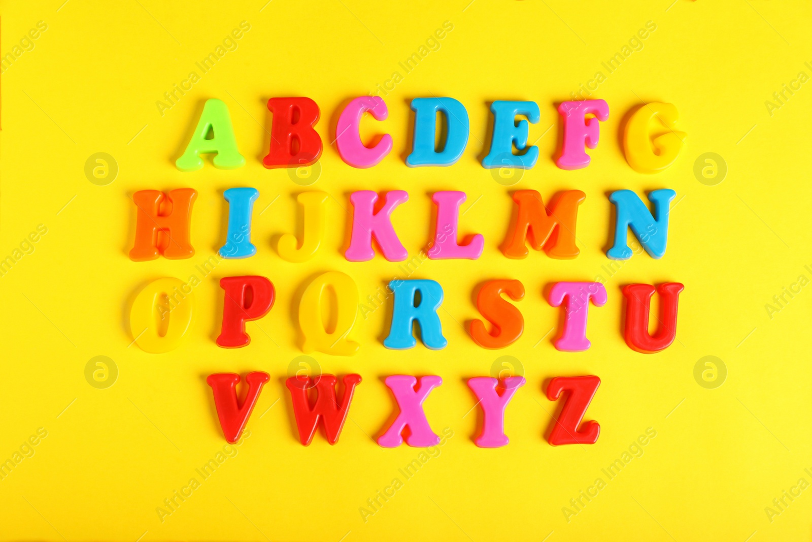 Photo of Plastic magnetic letters on yellow background, flat lay. Alphabetical order