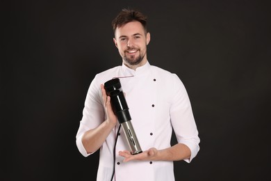 Photo of Smiling chef holding sous vide cooker on black background