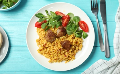 Photo of Plate of delicious rice pilaf with salad and cutlery on wooden background, top view