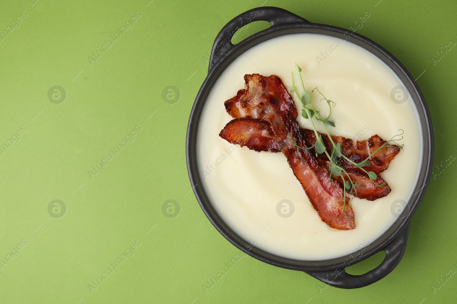 Photo of Delicious potato soup with bacon and microgreens in bowl on green table, top view. Space for text