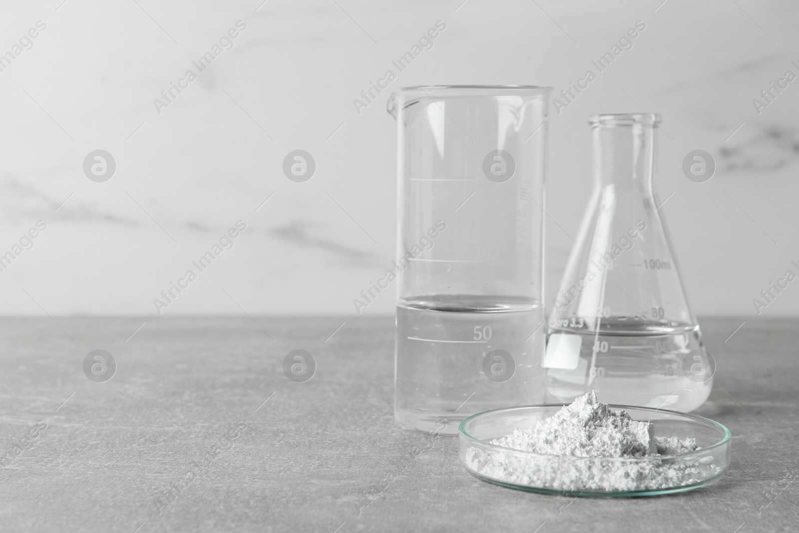 Photo of Petri dish with calcium carbonate powder and laboratory glassware on light grey table. Space for text