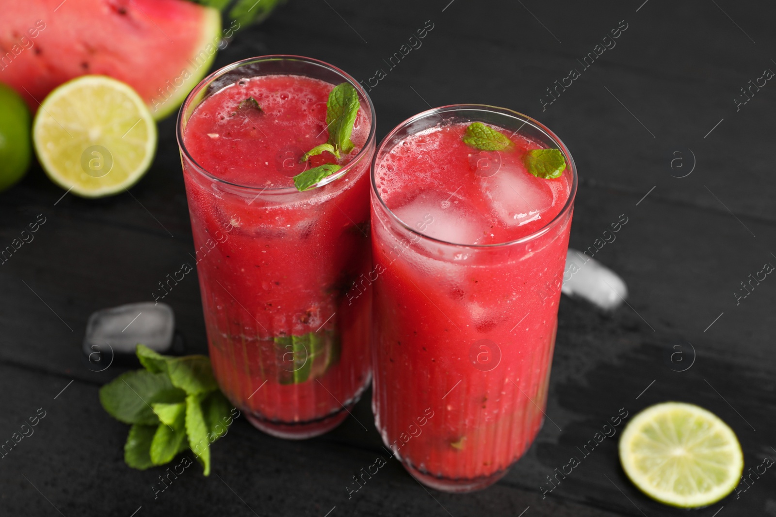 Photo of Glasses of delicious fresh watermelon juice, lime, mint and ice on black wooden table