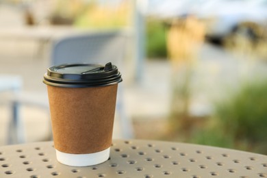 Paper cup with hot coffee on table outdoors, space for text. Takeaway drink