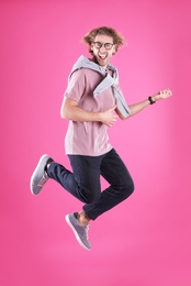 Young man playing air guitar on color background