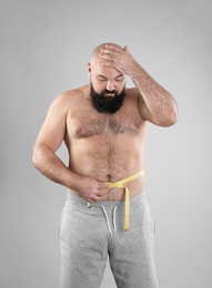 Fat man with measuring tape on grey background. Weight loss