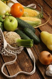 Photo of Different fresh vegetables in net bag on wooden table, closeup. Farmer harvesting