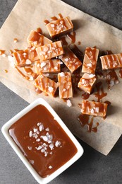 Tasty candies, caramel sauce and salt on grey table, top view