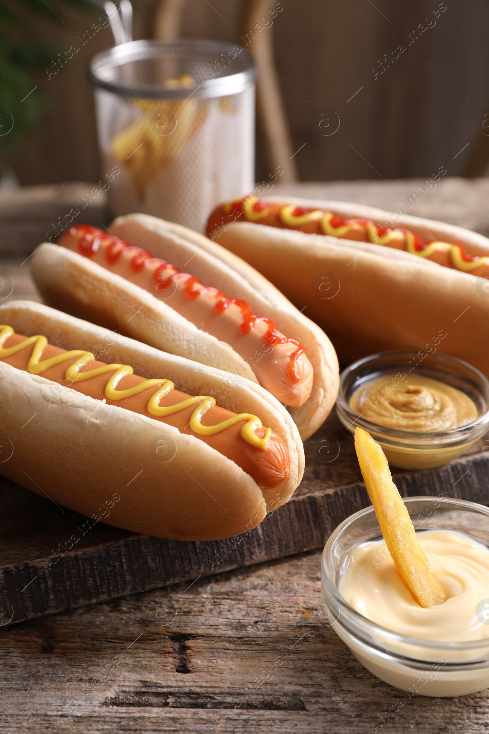 Photo of Delicious hot dogs with sauces and French fry on wooden table, closeup