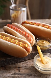 Photo of Delicious hot dogs with sauces and French fry on wooden table, closeup