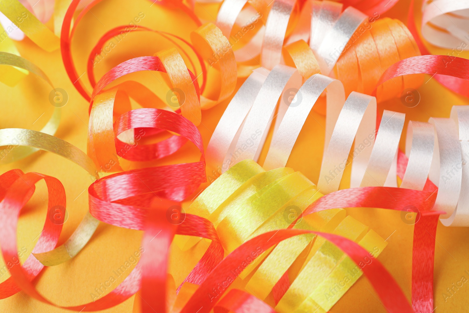 Photo of Colorful serpentine streamers on yellow background, closeup