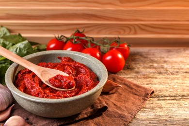 Photo of Bowl of tasty tomato paste with spoon and ingredients on wooden table. Space for text