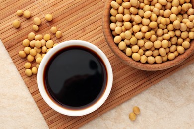 Photo of Soy sauce in bowl and soybeans on beige table, flat lay
