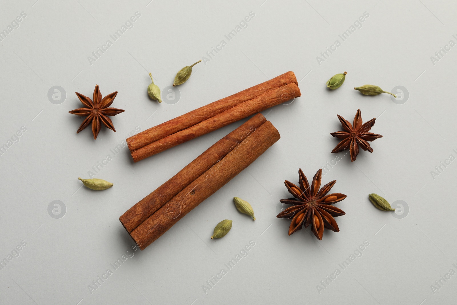 Photo of Cinnamon sticks, star anise and cardamom pods on light grey background, flat lay