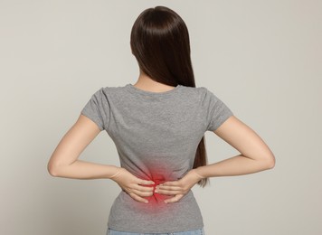 Woman suffering from pain in lower back on light background