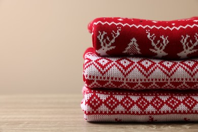 Photo of Stack of different Christmas sweaters on wooden table against beige background, closeup. Space for text