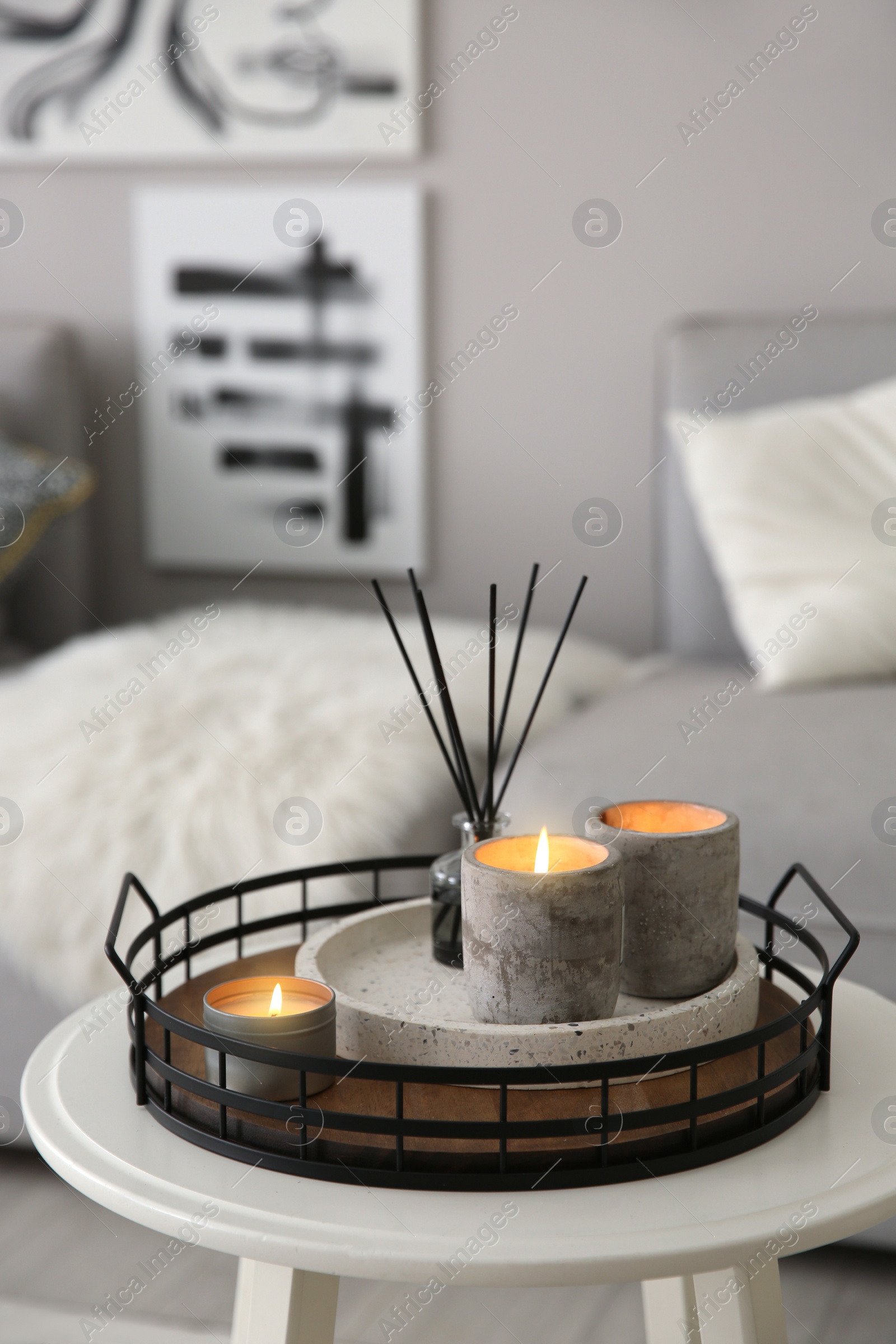 Photo of Candles and aroma reed diffuser on white table near grey sofa