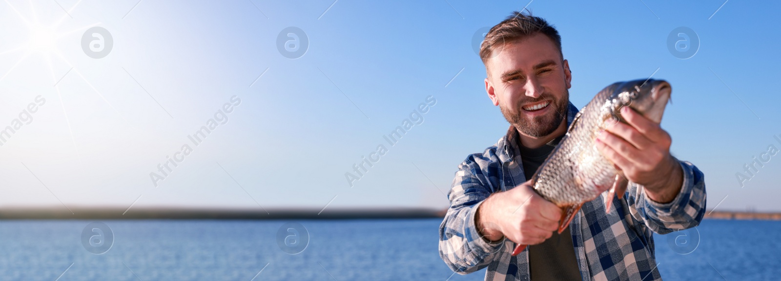 Image of Fisherman holding caught fish at riverside, space for text. Banner design