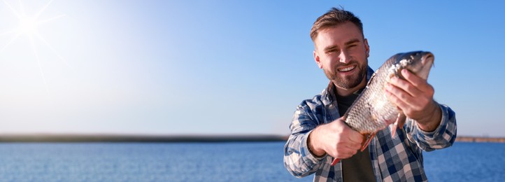 Image of Fisherman holding caught fish at riverside, space for text. Banner design