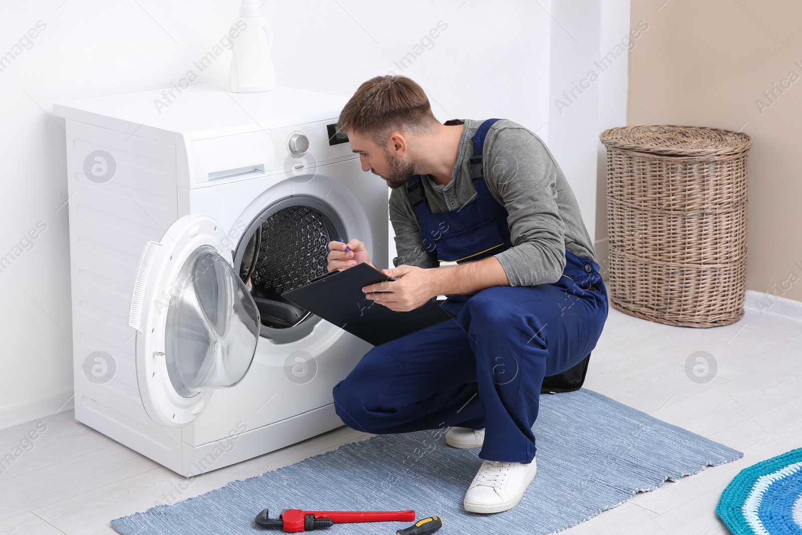 Photo of Young plumber with clipboard near washing machine in bathroom