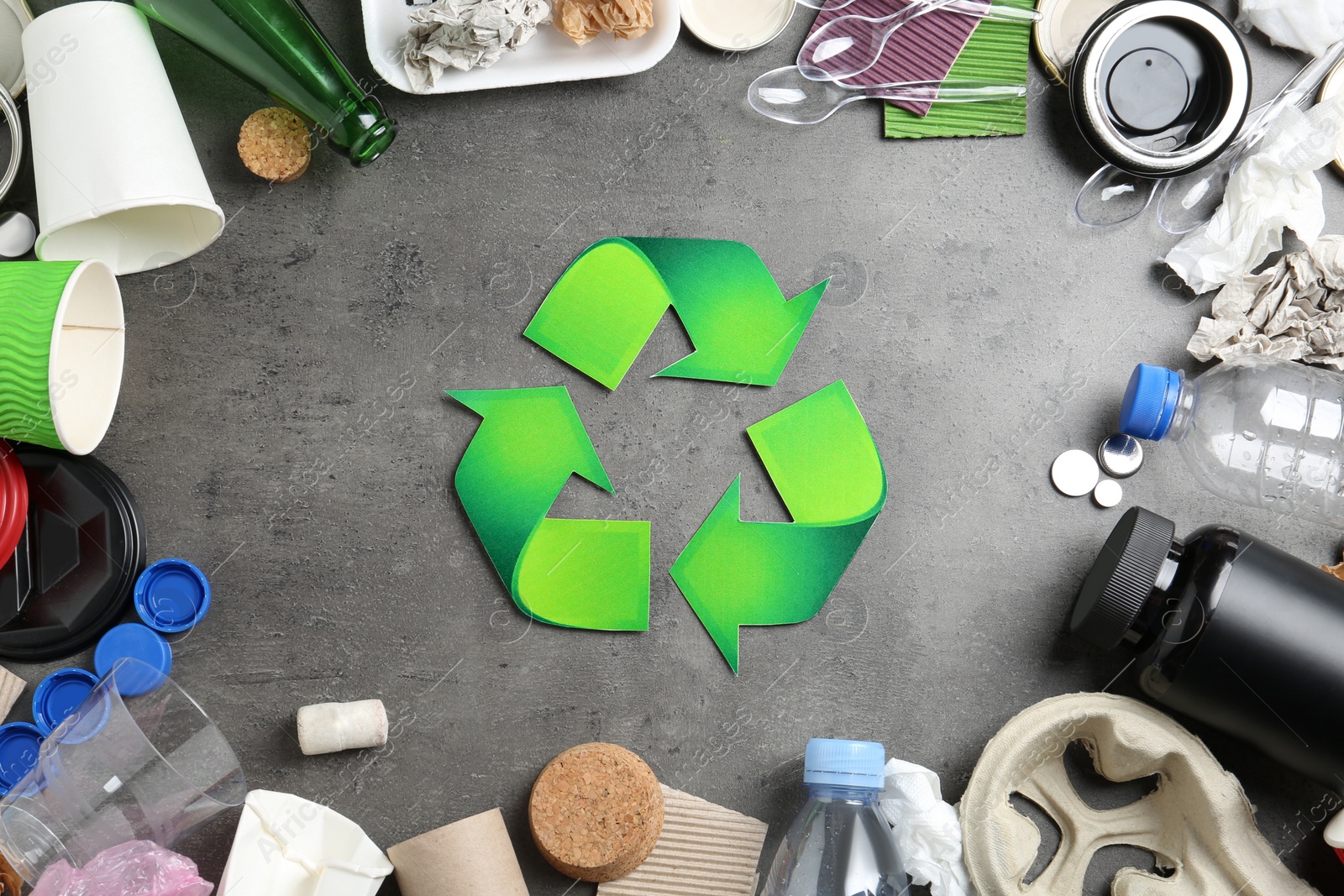 Photo of Recycling symbol and different garbage on gray background, top view