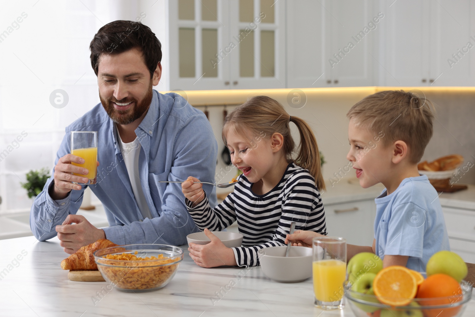 Photo of Father and his little children having breakfast at table in kitchen
