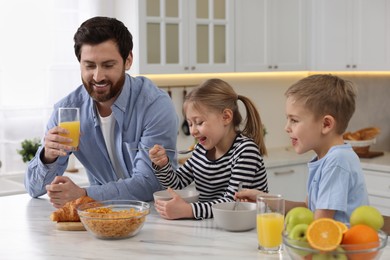 Father and his little children having breakfast at table in kitchen