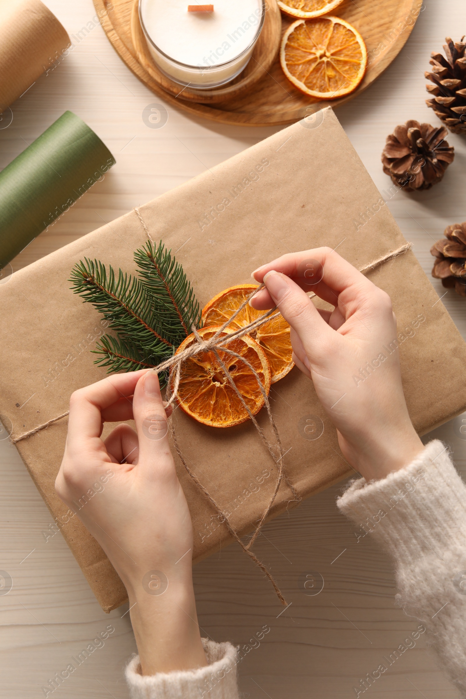 Photo of Woman decorating gift box with dry orange slices at white wooden table, top view