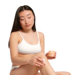 Photo of Beautiful young Asian woman applying body cream onto leg on white background